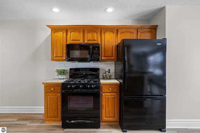 kitchen with decorative backsplash, black appliances, light countertops, and baseboards