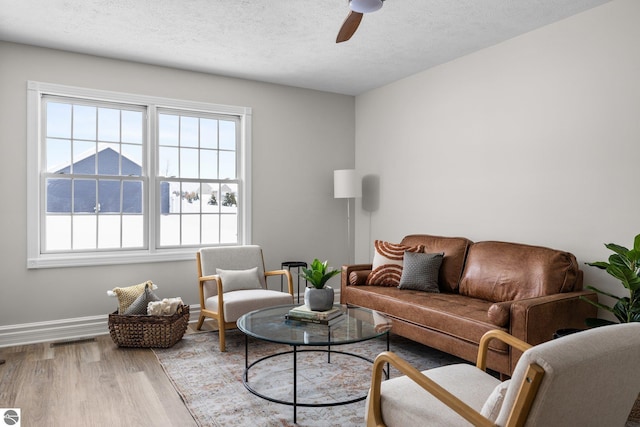 living area with visible vents, a textured ceiling, wood finished floors, baseboards, and ceiling fan