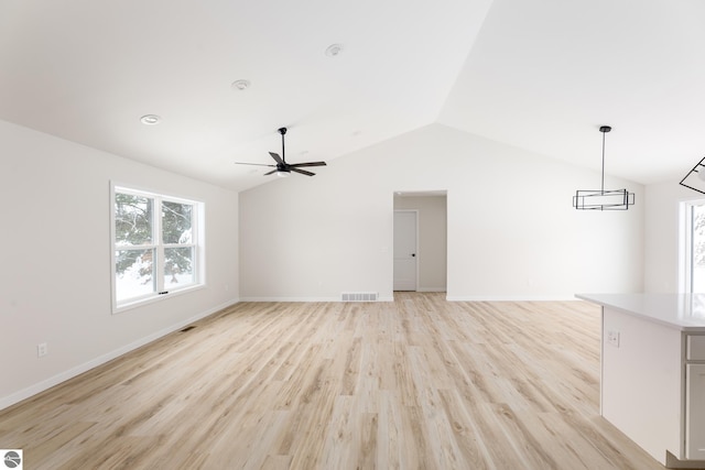 unfurnished living room featuring ceiling fan with notable chandelier, vaulted ceiling, and light wood-type flooring