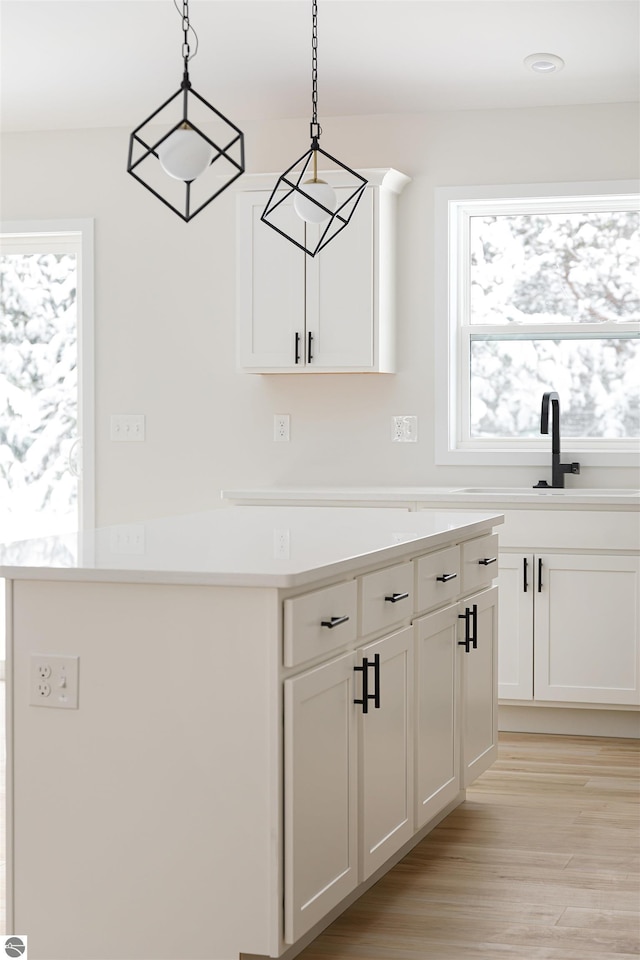 kitchen with white cabinetry, sink, decorative light fixtures, and light hardwood / wood-style floors