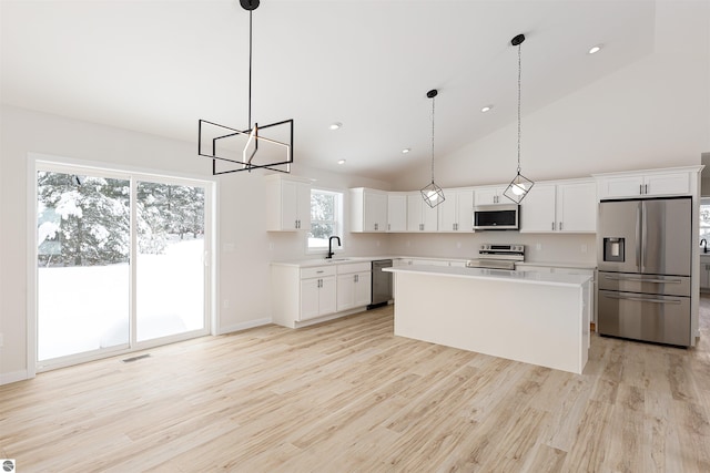 kitchen with appliances with stainless steel finishes, pendant lighting, white cabinets, a center island, and light hardwood / wood-style floors