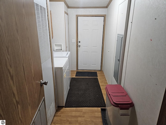 clothes washing area with ornamental molding, washer and dryer, a textured ceiling, and light hardwood / wood-style floors