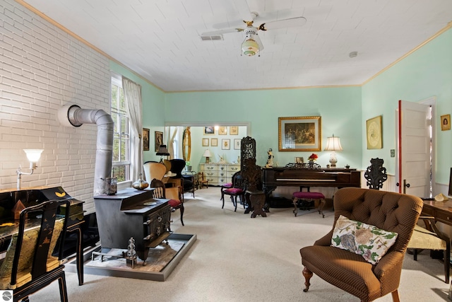 living area with brick wall, a wood stove, ceiling fan, crown molding, and light carpet