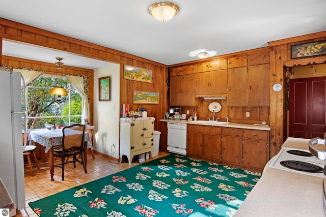 kitchen with light tile patterned flooring, sink, fridge, wooden walls, and white dishwasher