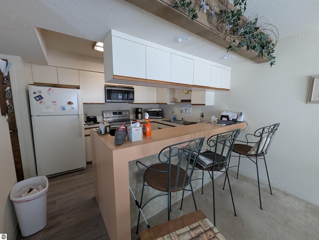 kitchen with a breakfast bar, sink, white cabinetry, appliances with stainless steel finishes, and kitchen peninsula