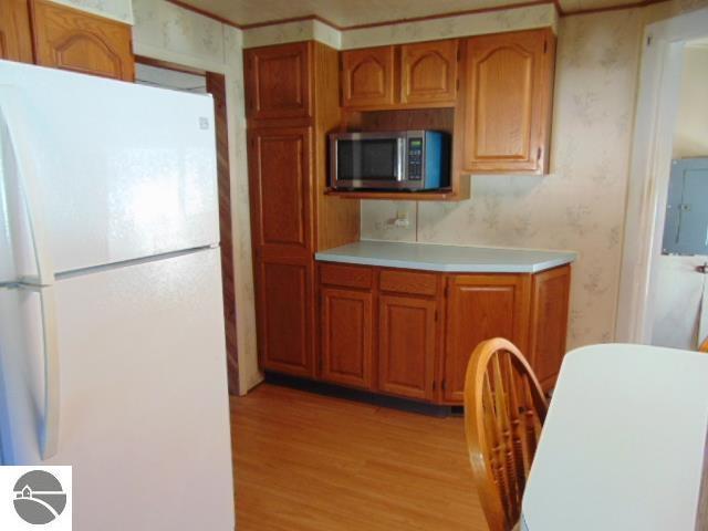 kitchen with freestanding refrigerator, light countertops, stainless steel microwave, electric panel, and light wood finished floors