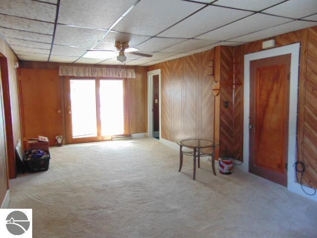 carpeted spare room featuring wooden walls, ceiling fan, and a drop ceiling