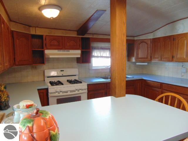 kitchen featuring open shelves, under cabinet range hood, white gas stove, and light countertops