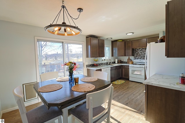 kitchen with dark brown cabinetry, sink, light wood-type flooring, pendant lighting, and white appliances