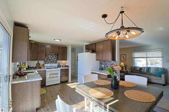 kitchen featuring white appliances, light hardwood / wood-style flooring, hanging light fixtures, dark brown cabinets, and tasteful backsplash