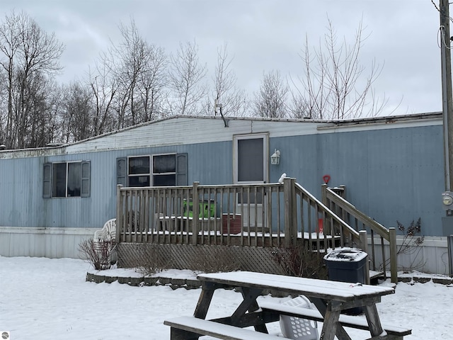 snow covered back of property with a wooden deck