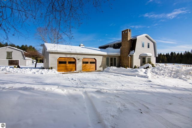 snow covered back of property featuring a garage