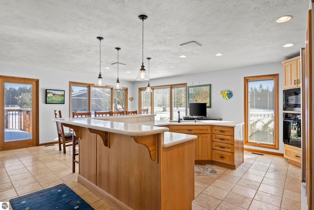 kitchen featuring a spacious island, a kitchen bar, light brown cabinetry, hanging light fixtures, and black appliances