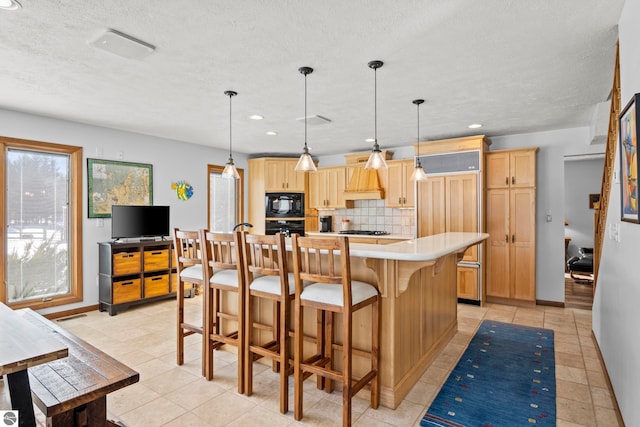 kitchen with hanging light fixtures, black appliances, an island with sink, and light brown cabinets