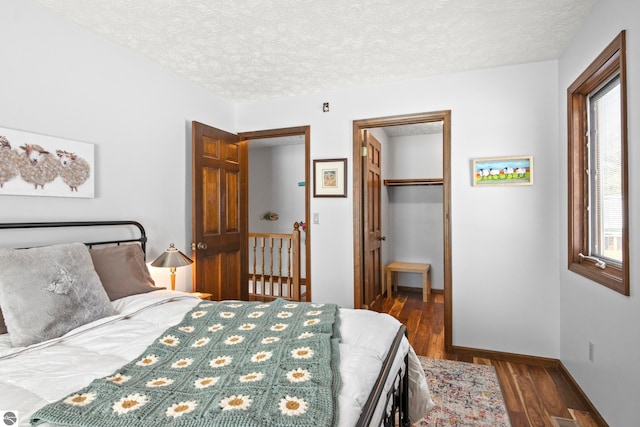 bedroom with dark wood-type flooring, a closet, a textured ceiling, and a walk in closet