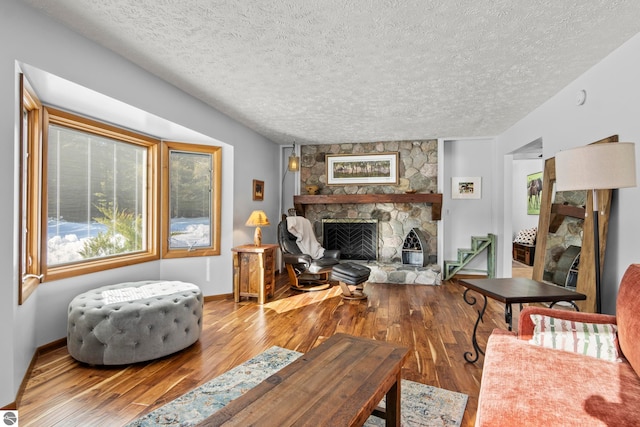 living room with a stone fireplace, wood-type flooring, and a textured ceiling