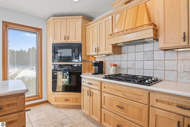 kitchen with light brown cabinets, light tile patterned floors, custom range hood, decorative backsplash, and black appliances