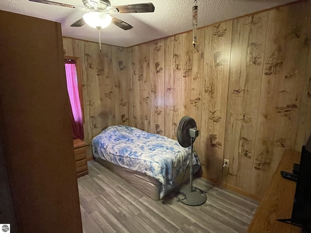 bedroom with hardwood / wood-style flooring, ceiling fan, wooden walls, and a textured ceiling