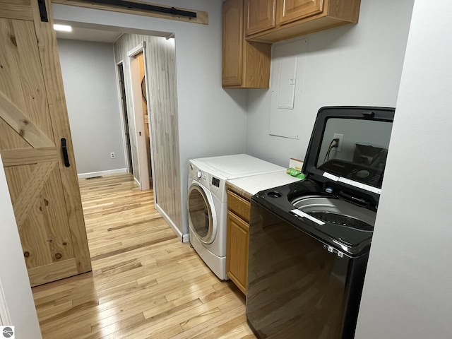 laundry area with cabinets, washing machine and clothes dryer, a barn door, and light wood-type flooring