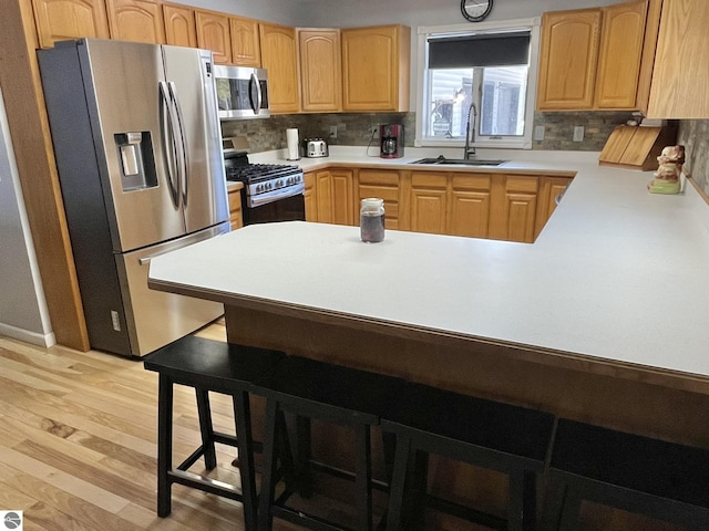 kitchen featuring appliances with stainless steel finishes, sink, light hardwood / wood-style floors, and decorative backsplash