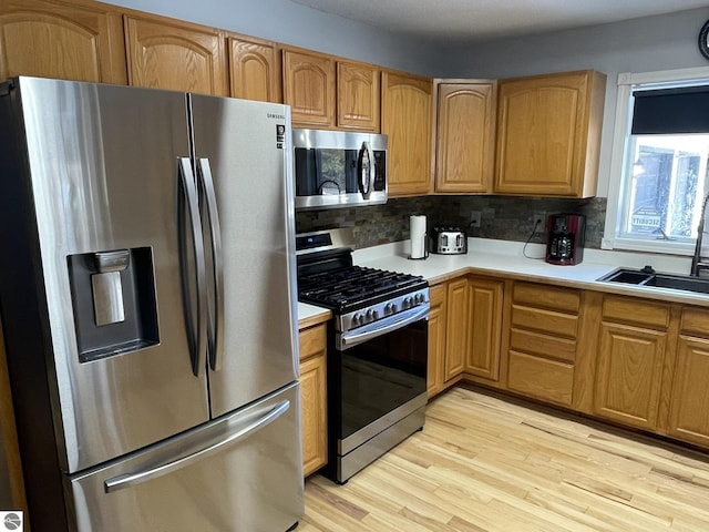 kitchen with sink, decorative backsplash, light wood-type flooring, and appliances with stainless steel finishes