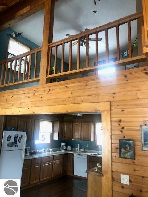 kitchen with a high ceiling, white appliances, and wood walls