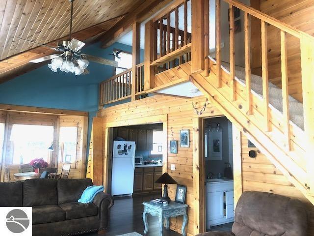 living room featuring ceiling fan, vaulted ceiling with beams, dark hardwood / wood-style floors, wooden ceiling, and wood walls