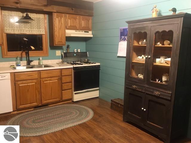 kitchen featuring dark wood-type flooring, white appliances, wooden walls, and sink