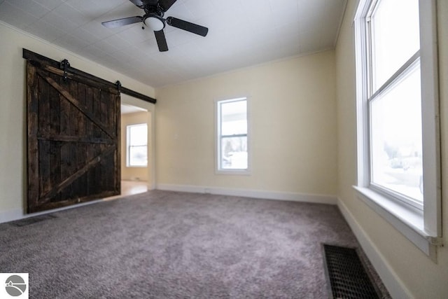 empty room featuring a barn door, ceiling fan, and carpet flooring