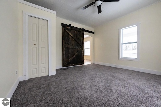 interior space featuring crown molding, a barn door, ceiling fan, and dark colored carpet