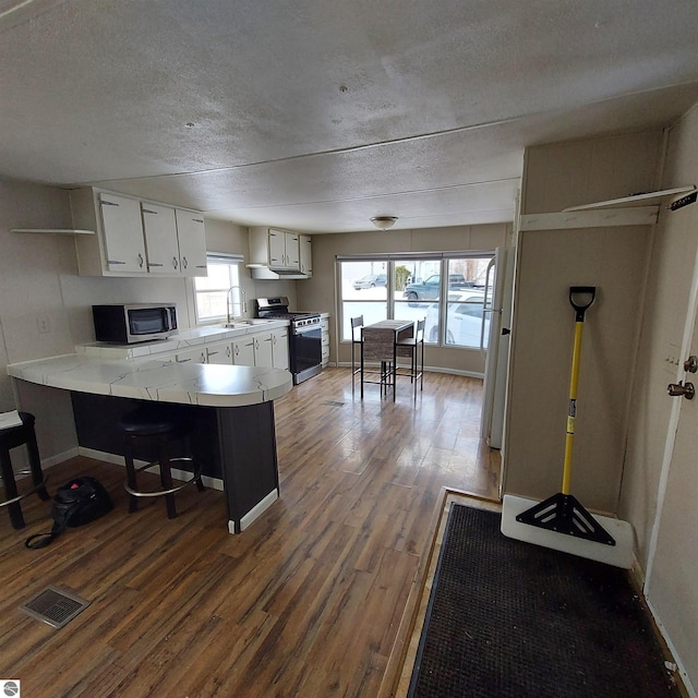 kitchen with white cabinetry, a breakfast bar area, dark hardwood / wood-style flooring, kitchen peninsula, and stainless steel appliances