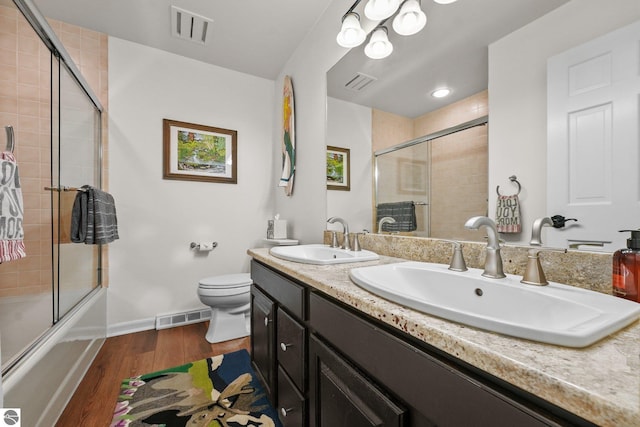 full bathroom with vanity, hardwood / wood-style flooring, combined bath / shower with glass door, and toilet