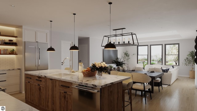 kitchen with stainless steel built in refrigerator, sink, light wood-type flooring, an island with sink, and light stone countertops