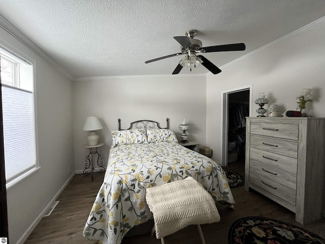 bedroom with ornamental molding, a walk in closet, dark wood-type flooring, and a textured ceiling