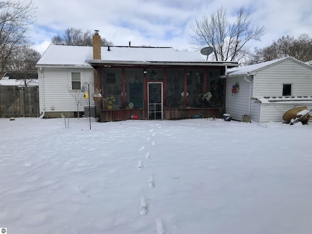 snow covered rear of property featuring a sunroom