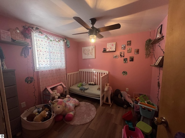 bedroom featuring a nursery area, ceiling fan, and wood-type flooring