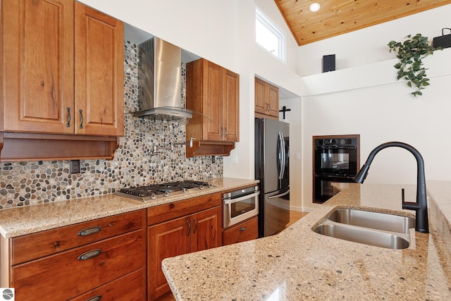 kitchen with sink, light stone counters, appliances with stainless steel finishes, decorative backsplash, and wall chimney range hood