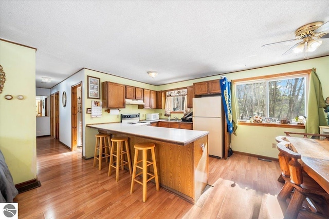 kitchen featuring white appliances, light hardwood / wood-style flooring, kitchen peninsula, and a textured ceiling