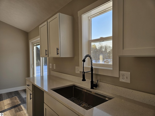 kitchen with sink, white cabinetry, light stone countertops, dark hardwood / wood-style flooring, and vaulted ceiling