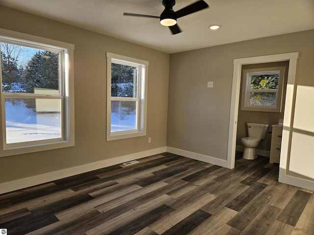 unfurnished bedroom with ceiling fan, ensuite bathroom, dark hardwood / wood-style floors, and multiple windows