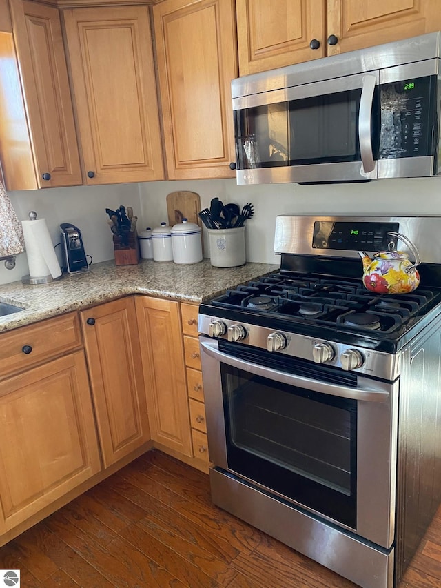 kitchen with light stone counters, appliances with stainless steel finishes, and dark hardwood / wood-style floors