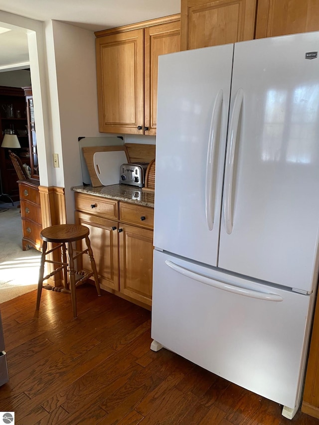 kitchen with light stone counters, dark wood-type flooring, and white fridge