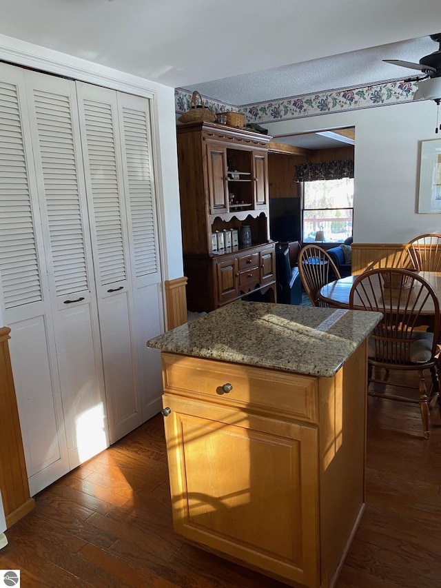 kitchen featuring stone counters, a kitchen island, dark hardwood / wood-style floors, ceiling fan, and a textured ceiling