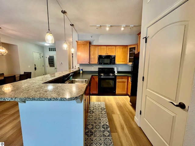 kitchen featuring sink, light hardwood / wood-style flooring, hanging light fixtures, kitchen peninsula, and black appliances