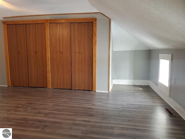 additional living space featuring lofted ceiling, dark hardwood / wood-style floors, and a textured ceiling