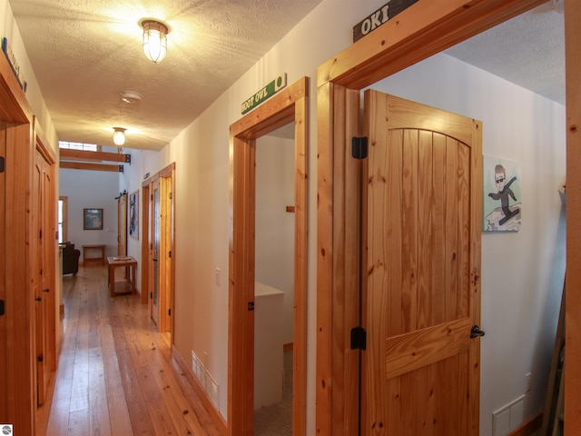 corridor with a textured ceiling and light hardwood / wood-style flooring