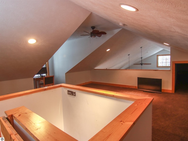 interior space featuring ceiling fan, vaulted ceiling, a textured ceiling, and dark colored carpet