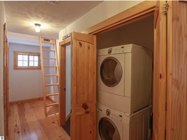 clothes washing area featuring stacked washer / dryer, a textured ceiling, and light wood-type flooring