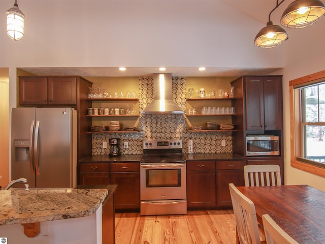 kitchen featuring wall chimney exhaust hood, tasteful backsplash, light hardwood / wood-style flooring, appliances with stainless steel finishes, and dark stone counters