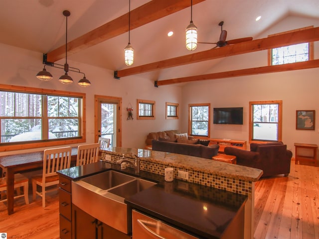 kitchen with lofted ceiling with beams, an island with sink, sink, hanging light fixtures, and light hardwood / wood-style floors